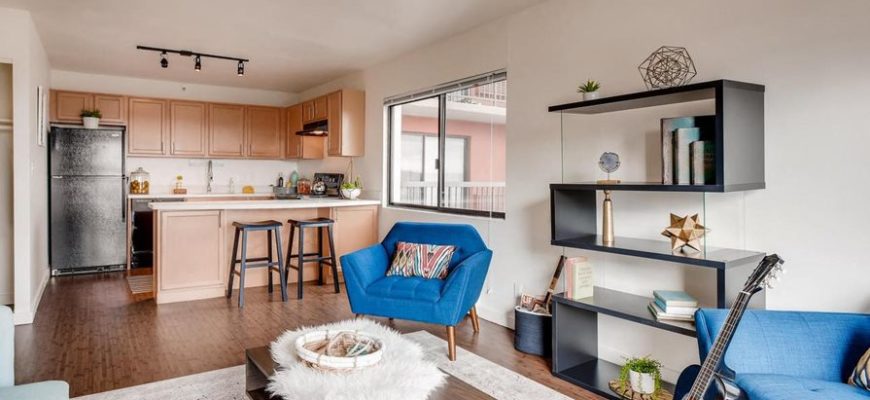 modern living room with a guitar leaning on a couch, a coffee table with a furry basket, a love seat, bar stools in the background and a wall zigzag bookcase.