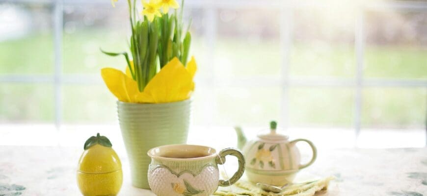 A Table in Front of a Large Window with a teapot, teacup, and a Vase with Flowers